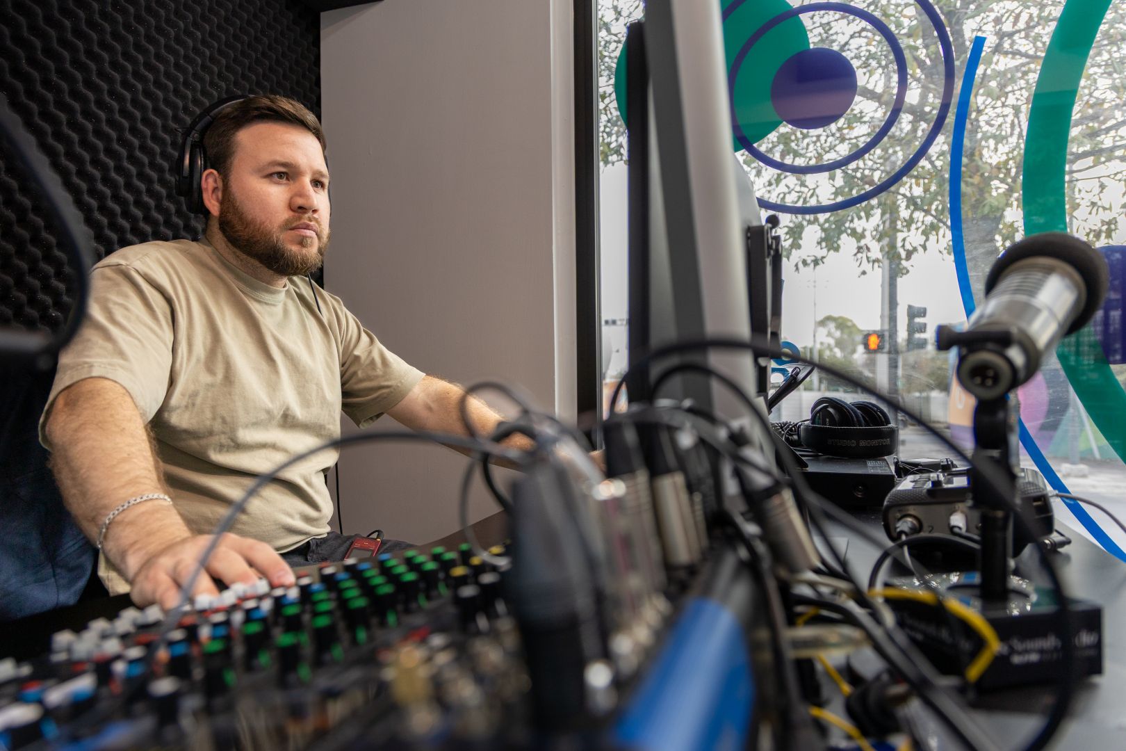 Operador de audio con audífonos manipula la consola durante una transmisión en cabina de radio.