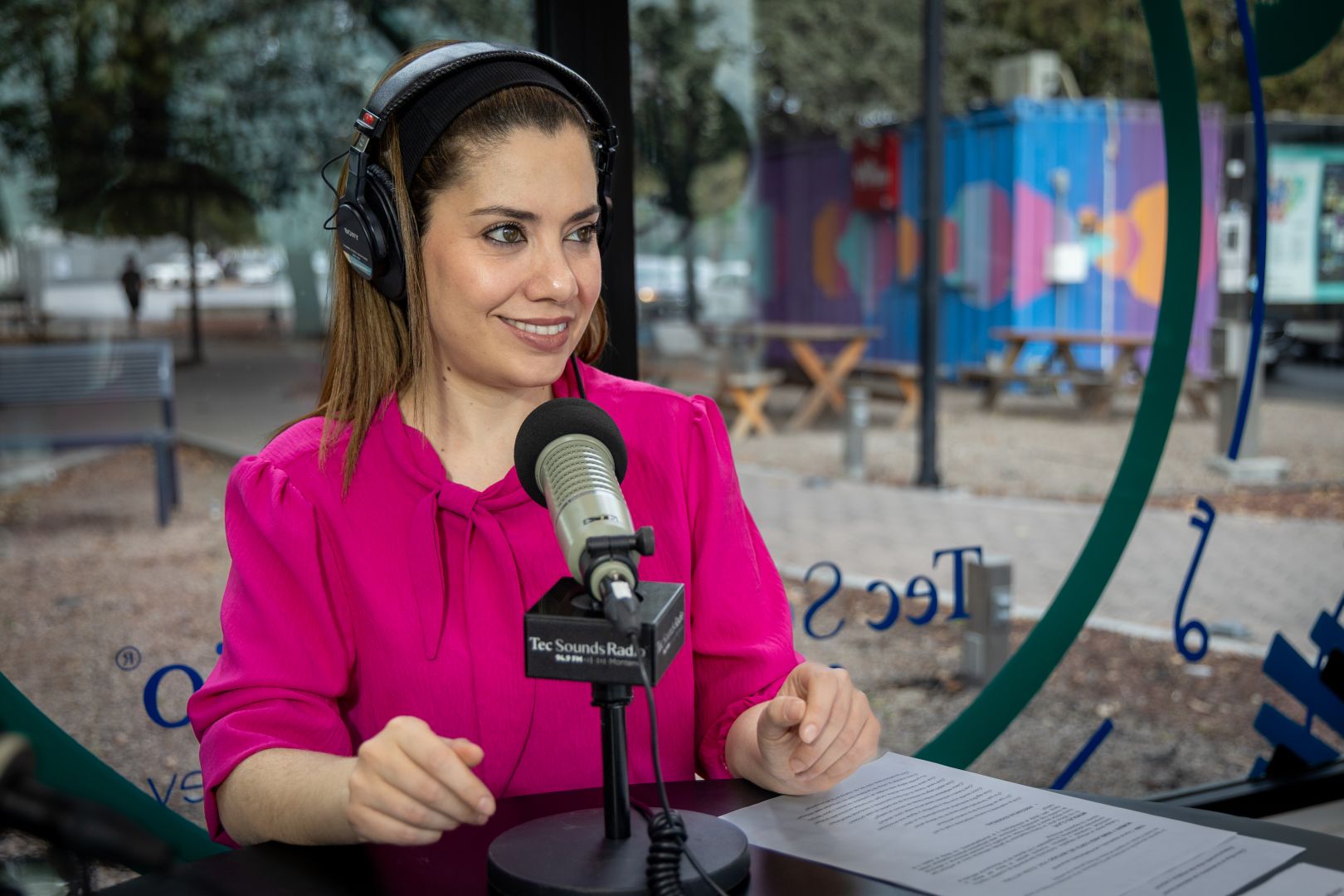 Conductora de radio con audífonos habla frente a un micrófono de Tec Sounds Radio durante la grabación del programa.