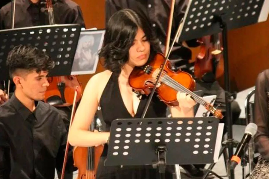 Joven mujer vestida de negro hace m&uacute;sica tocando el viol&iacute;n en una orquesta