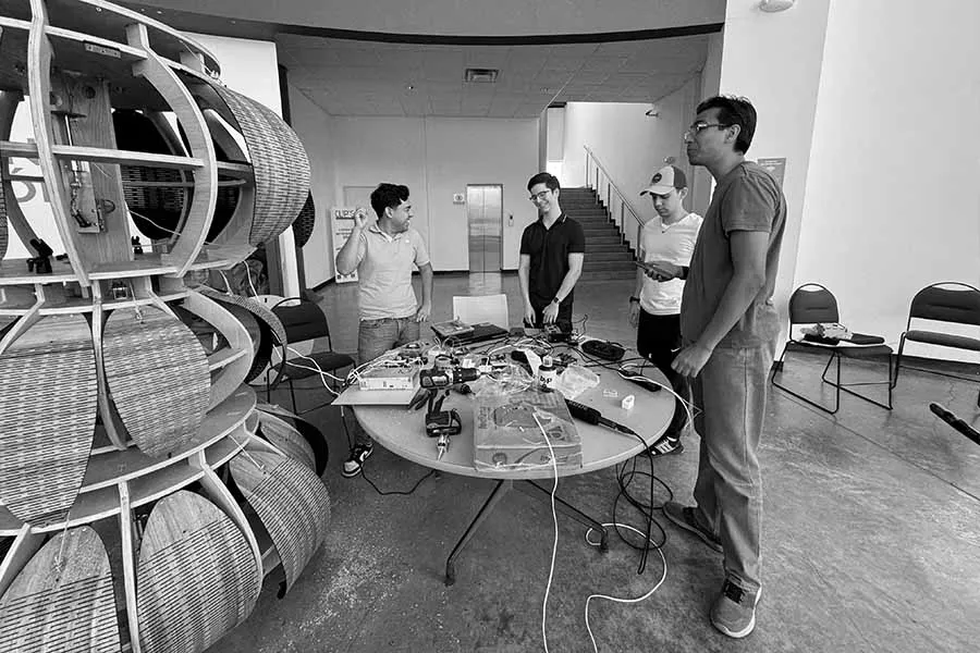 Cuatro j&oacute;venes frente a una mesa con equipo t&eacute;cnico y una escultura al lado.