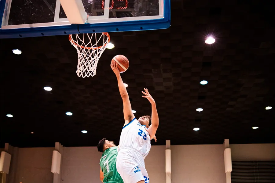 Jugador de Borregos Laguna est&aacute; por encestar el bal&oacute;n de b&aacute;squebtol ante la defensa de atleta vestido de verde