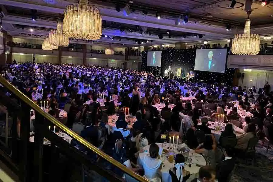 Vista en picada de un sal&oacute;n de eventos con mesas llenas de asistentes. 