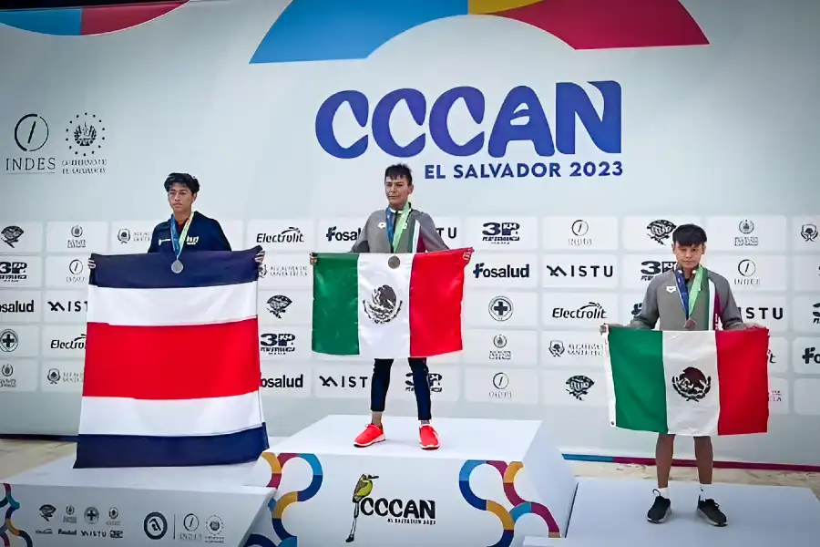 Diego Lizardi, nadador hidalguense, en el podio con la medalla de oro en el CCCAN El Salvador 2023, sosteniendo la bandera de M&eacute;xico junto a los medallistas de Costa Rica y M&eacute;xico.