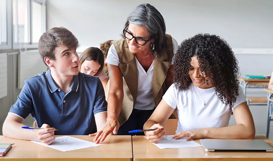Profesora en sal&oacute;n de clases asesorando alumnos en su trabajo.