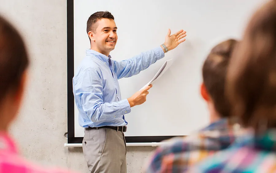 Profesor explicando la clase frente a un pizarr&oacute;n.