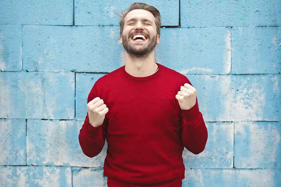 humbre con sudadera roja, con las manos al  nivel del pecho, pu&ntilde;os cerrados y sonriendo