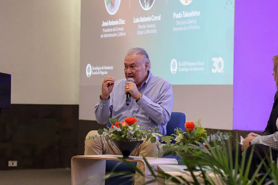 Hombre sentado en escenario hablando al p&uacute;blico. 
