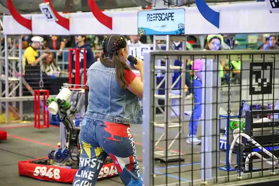 Vista de espaldas de una jov&eacute;n en la cancha de FIRST presentando a los equipos.