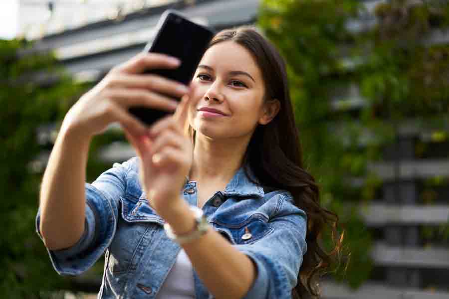 Mujer tom&aacute;ndose una selfie con su celular en un espacio abierto.