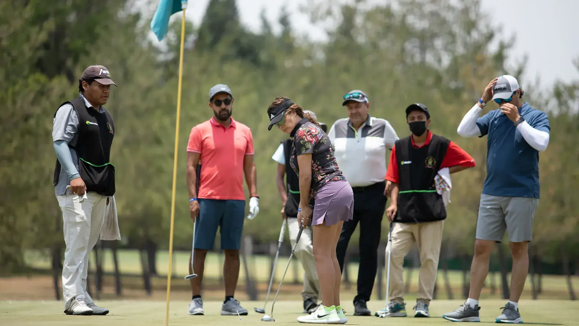 Grupo de golfistas viendo a una jugadora intentar un putt