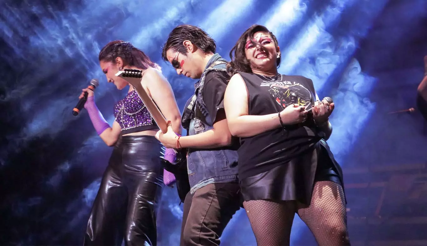 Alumno tocando la guitarra con una cantante a cada lado en poses rockeras como parte del Ensamble IMMORTALITY.