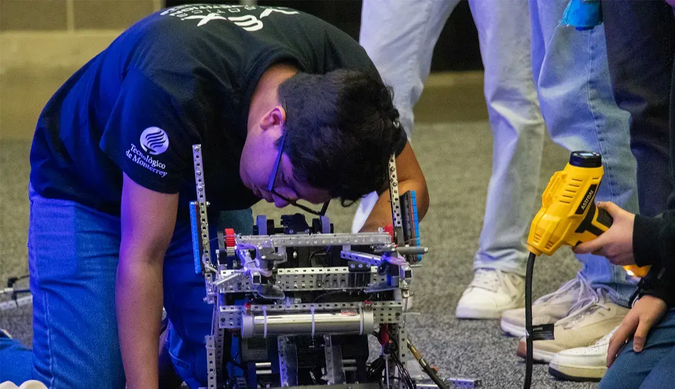 Alumno agachado reparando un robot.