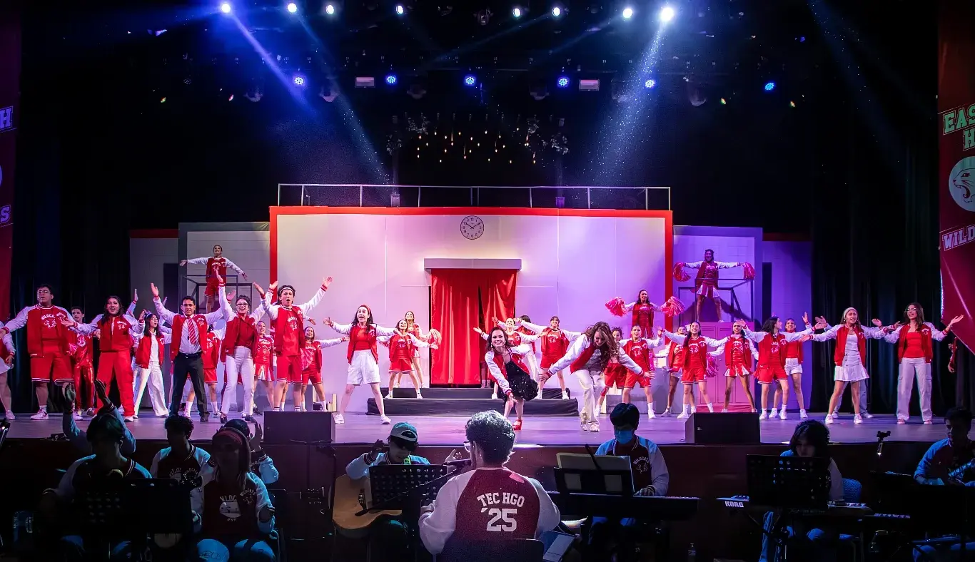 El elenco completo interpreta el número final del musical High School Musical: On Stage, mientras al frente se distingue al director del ensamble musical guiando a los músicos del campus Hidalgo.