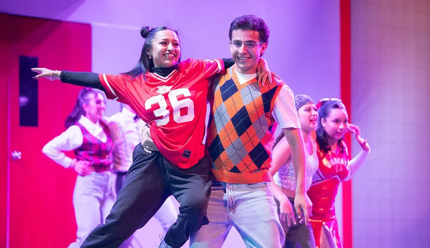 Pareja de estudiantes caracterizados como skater y nerd interpretan un número de baile durante High School Musical: On Stage, como parte del elenco artístico estudiantil.