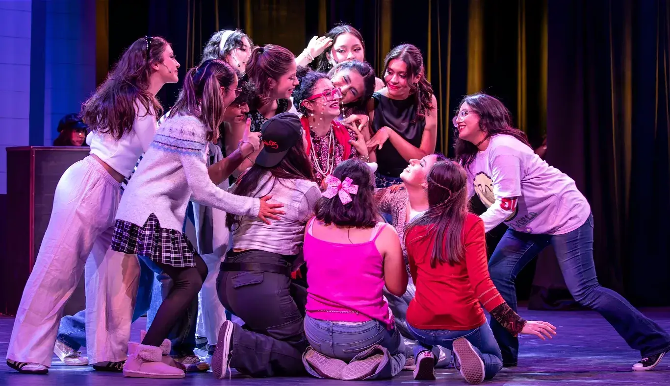 Estudiantes interpretan una escena de la clase de teatro dirigida por la señora Darbus durante el musical High School Musical: On Stage, caracterizados con vestuario expresivo y actitudes teatrales.