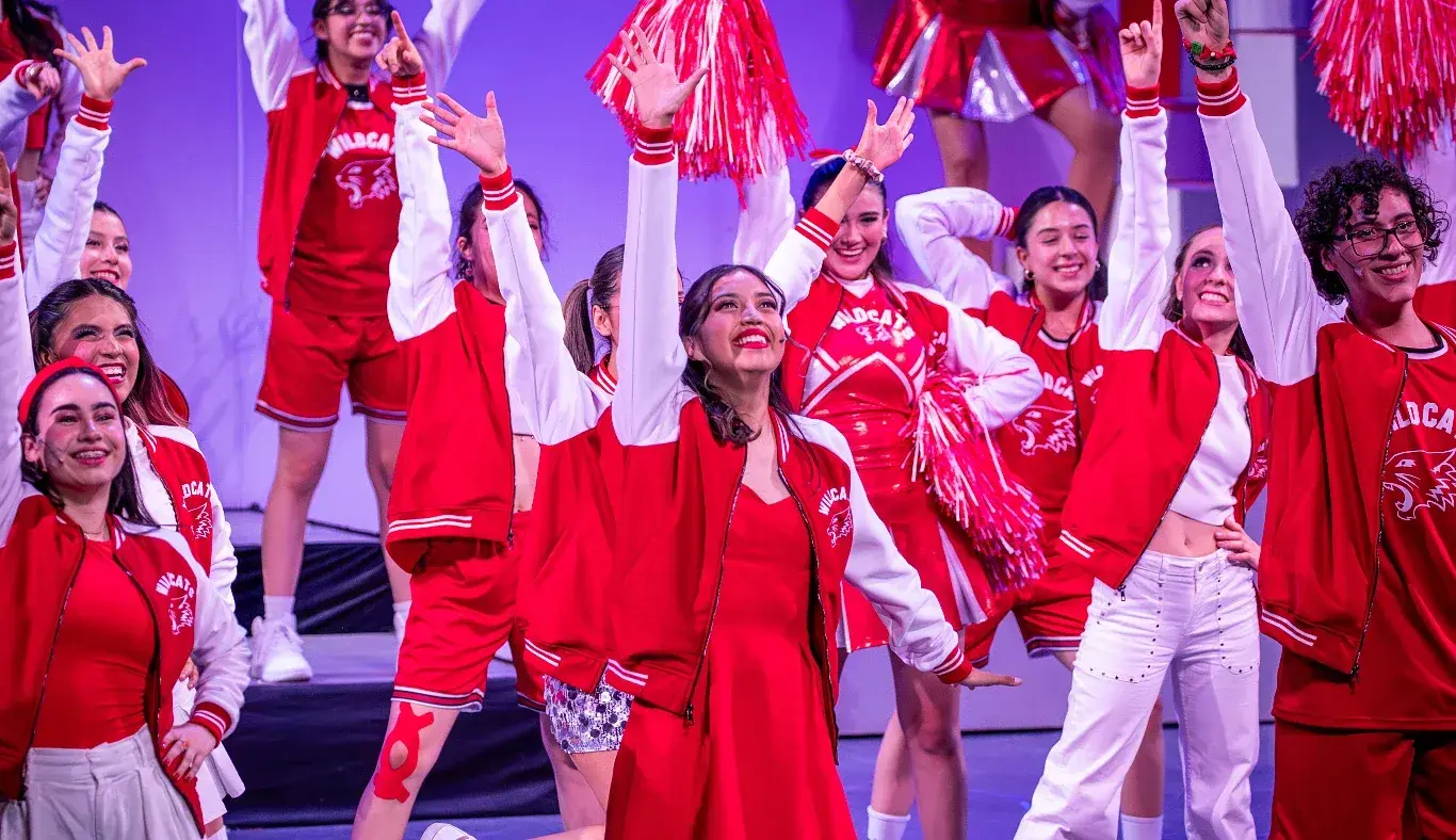 Gabriella, al centro del escenario, lidera al elenco durante el número final de High School Musical: On Stage, con vestuarios rojos y coreografía grupal del equipo Wildcats.