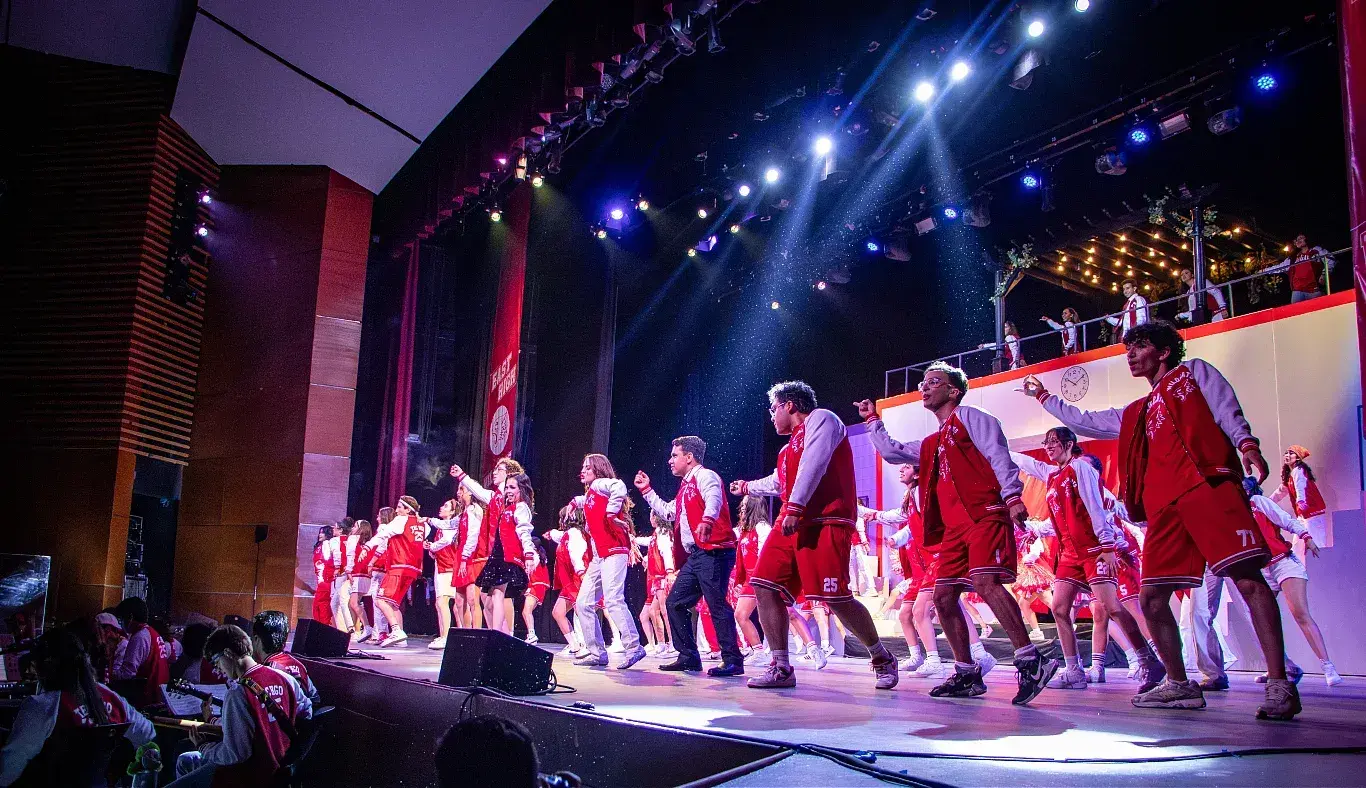 Elenco completo de High School Musical: On Stage interpreta el número final sobre el escenario del campus Hidalgo, con escenografía iluminada, coreografía grupal y ambientación escénica.