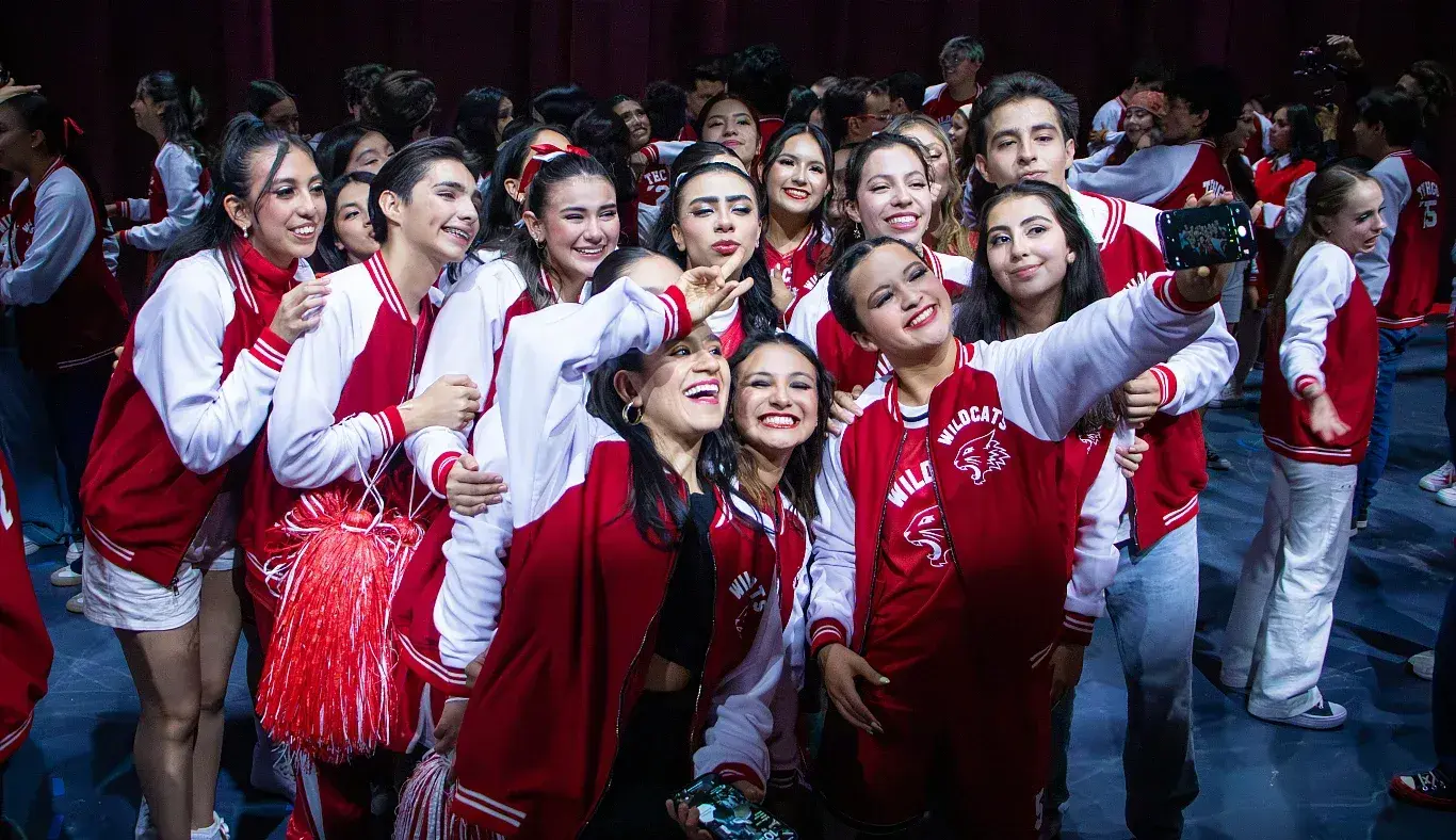 Integrantes del elenco de High School Musical: On Stage se toman una selfie grupal en el escenario tras finalizar la función, con vestuario del equipo Wildcats y expresiones de alegría.