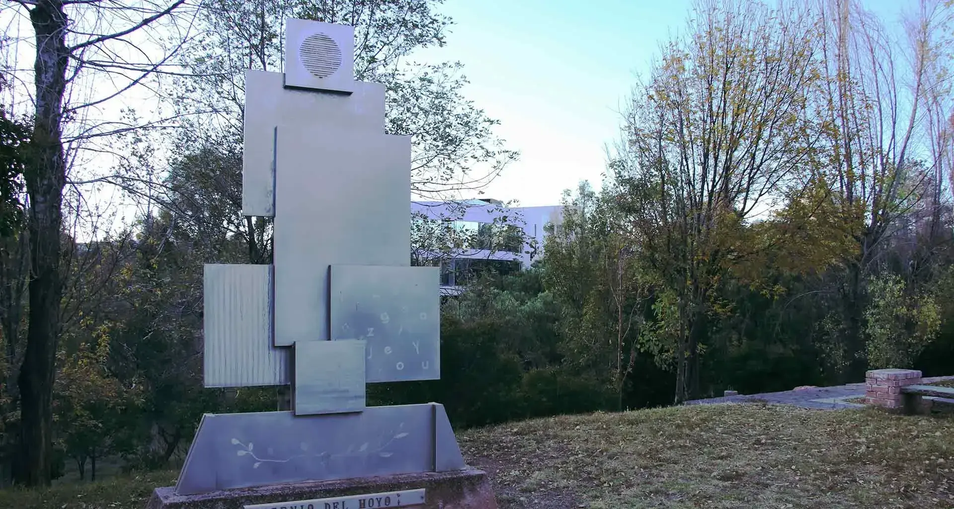 Imagen del monumento en Memoria a Don Eugenio del Hoyo, a un costado de cafeteria, se muestran varias figuras rectangulares, acomodadas una sobre la otra y articuladas verticalmente.