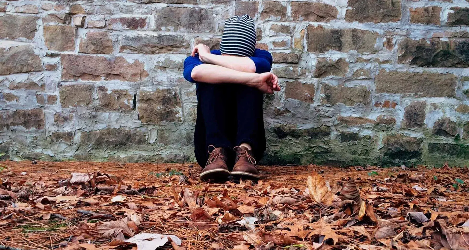 Joven sentado en el piso cubriendo su cabeza con los brazos.