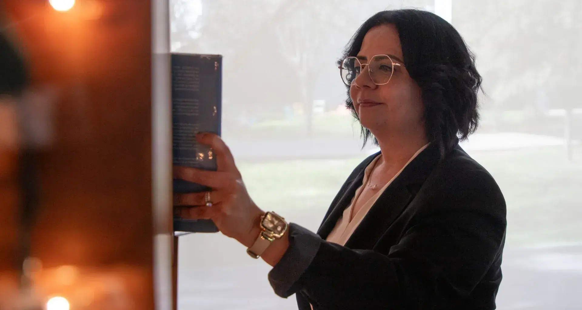 Directora de Mentoría de PrepaTec Laguna con vestimenta profesional toma libro de estante