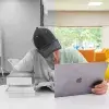 Joven observando un libro y una computadora