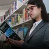 Profesor leyendo libro recargado contra un librero