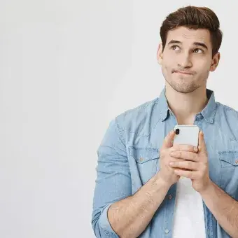 Consejos para no sentirte solo esta cuarentena. En la foto aparece un joven pensativo con su celular en mano