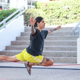 Mujer sentada sobre la cuerda floja con una pierna extendida sobre ella. 