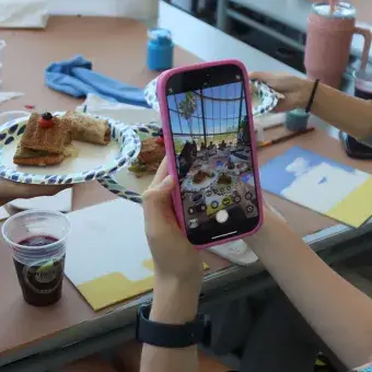 Chica tomando una foto con su celular de una mesa cubierta con comida y lienzos.