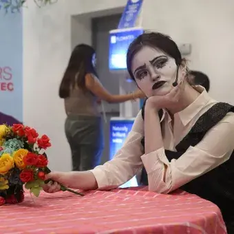 Chica recargada en una mesa con expresión pensativa y maquille dramático en blanco y negro.