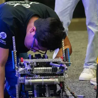Alumno agachado reparando un robot.