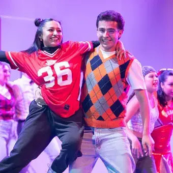 Pareja de estudiantes caracterizados como skater y nerd interpretan un número de baile durante High School Musical: On Stage, como parte del elenco artístico estudiantil.