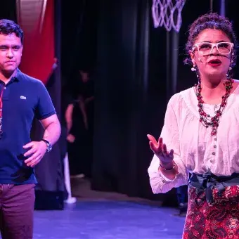 Estudiantes interpretan una escena de confrontación entre el entrenador Bolton y la señora Darbus durante el musical High School Musical: On Stage, con elementos representativos del deporte y el teatro.