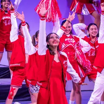 Gabriella, al centro del escenario, lidera al elenco durante el número final de High School Musical: On Stage, con vestuarios rojos y coreografía grupal del equipo Wildcats.
