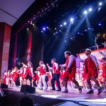 Elenco completo de High School Musical: On Stage interpreta el número final sobre el escenario del campus Hidalgo, con escenografía iluminada, coreografía grupal y ambientación escénica.