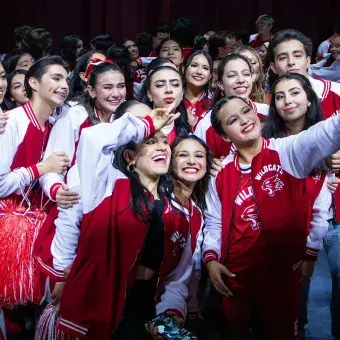 Integrantes del elenco de High School Musical: On Stage se toman una selfie grupal en el escenario tras finalizar la función, con vestuario del equipo Wildcats y expresiones de alegría.