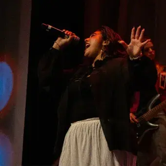 Chica cantando en escenario con top negro y falda blanca.