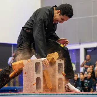 Profesor de Tae Kwon Do rompiendo una tabla de madera que descansa sobre dos ladrillos con la plama de su mano.