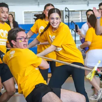 Alumnos universitarios vestidos de amarillo jalando una cuerda. 