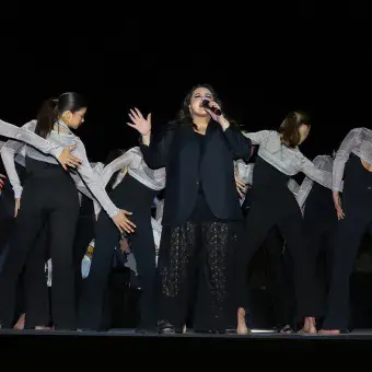 Cantante en escenario con bailarines atrás. 