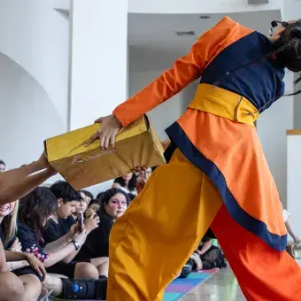Actriz vestida de colores jala caja que sostiene un miembro del público.