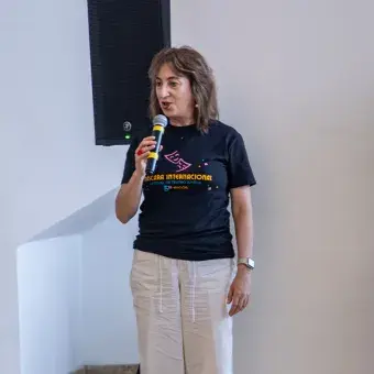 Dos mujeres paradas frente a un público mientras una sostiene un micrófono.