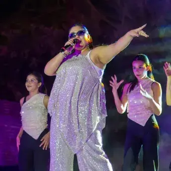 Cantante vetida de blanco con bailarinas detrás de ella. 