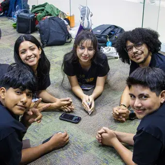 5 jóvenes ascostado en cículo viendo hacia la cámara. 