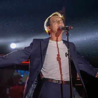 Cantante frente a micrófono con los brazos abiertos. 
