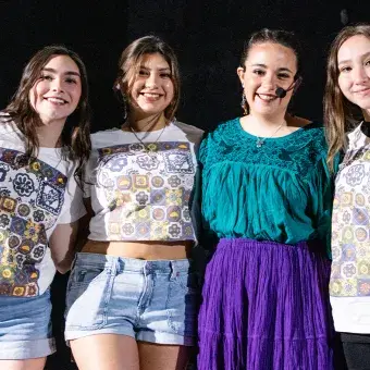 Cuatro chicas abrazadas sobre el escenario viendo a la cámara.