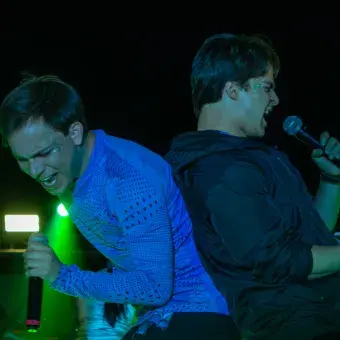 Dos hombres cantando recargados espalda contra espalda.